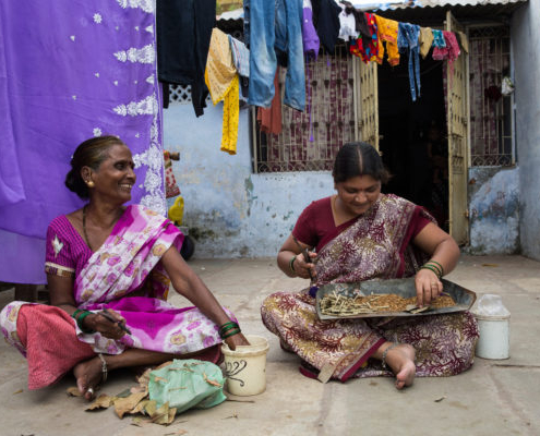Mother and daughter sit on the floor of their home hand rolling Indian-style cigarettes called bidi