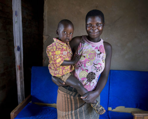A woman smiling and holding her young child in Uganda