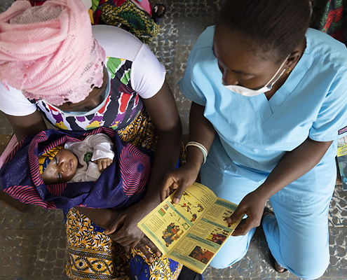 A community health nurse gives medical advice to a mother holding an infant in Sierra Leone