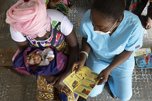 A community health nurse gives medical advice to a mother holding an infant in Sierra Leone