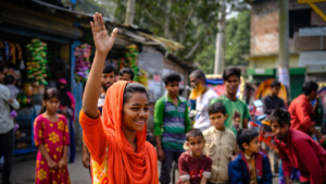 Girl waving at an outdoor puppet show in Bangladesh
