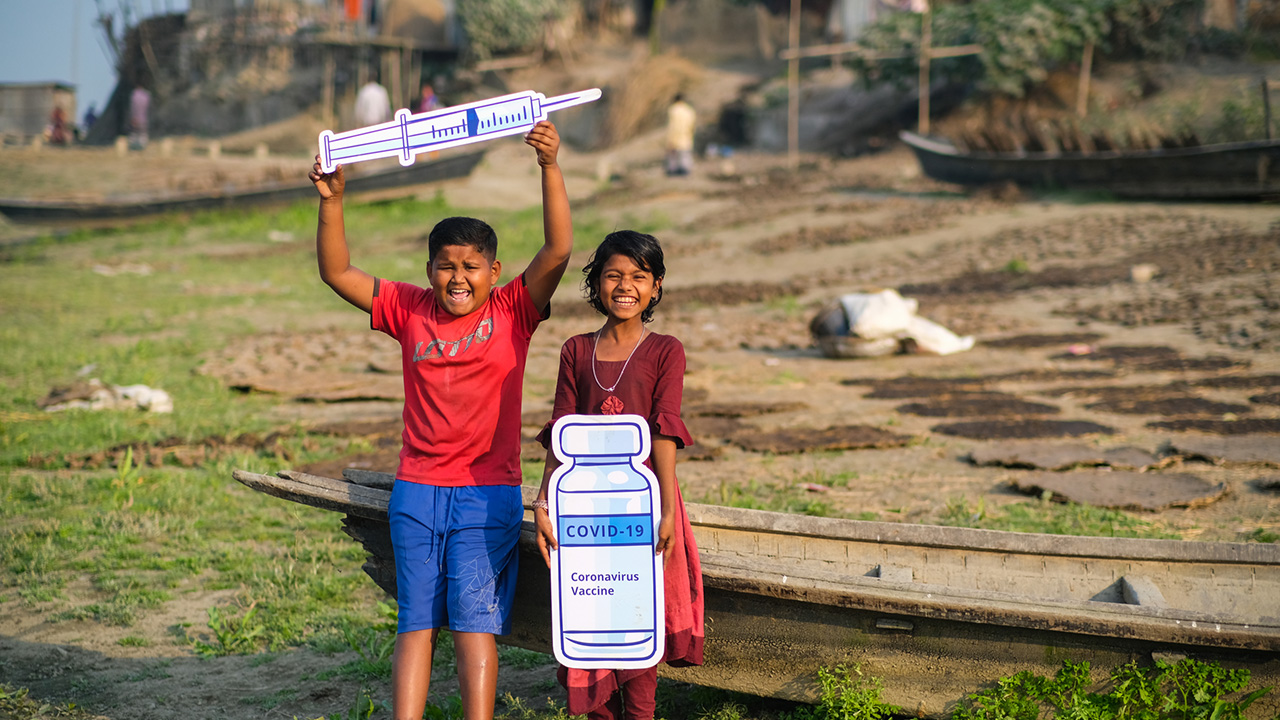 A 13 year old boy and 12 year old girl with signs about getting the COVID-19 vaccine in Bangladesh