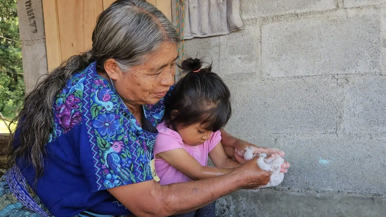 A Guatemalan grandmother washes the hands of her grandchild