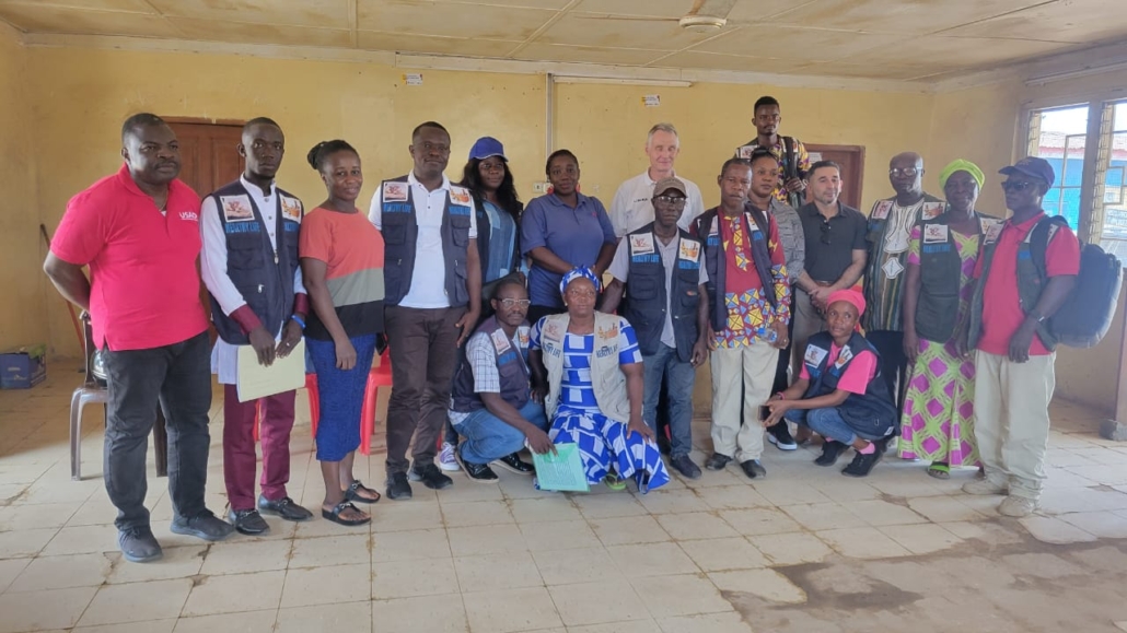 USAID Liberia Mission Director posing for a photo with members of a health advocacy committee in Bomi County, Liberia.