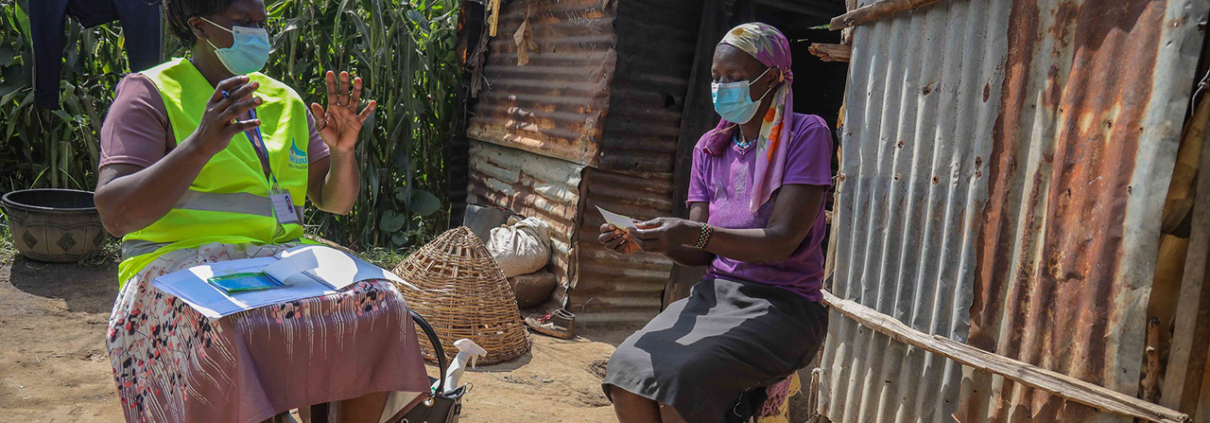 A female community health worker and a woman sit outside during a home visit in Kenya