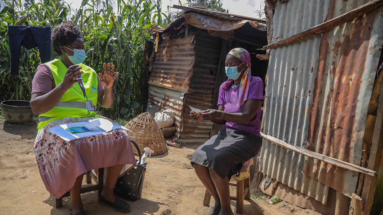 A female community health worker and a woman sit outside during a home visit in Kenya