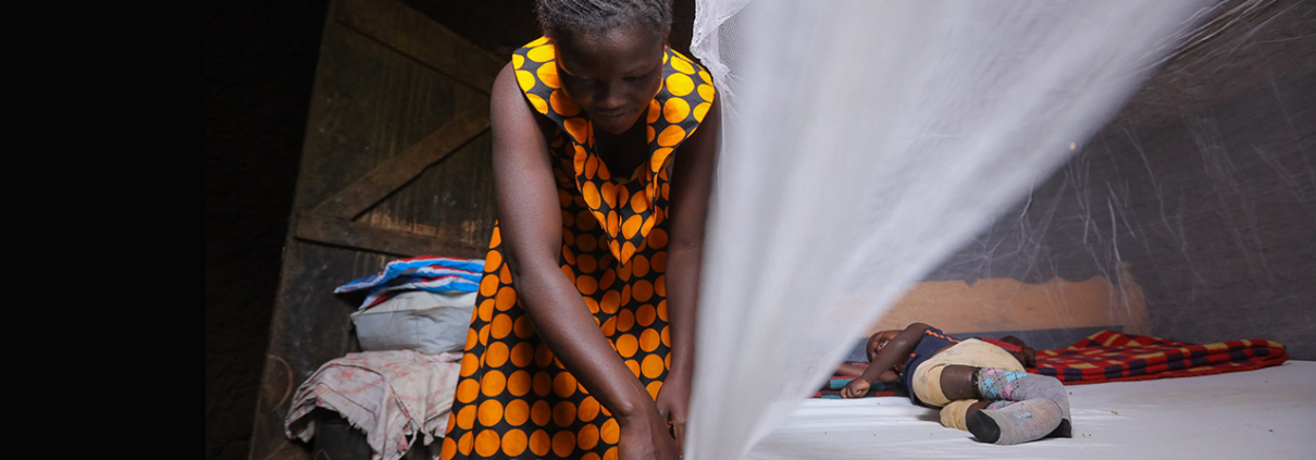 A mother secures her child under a mosquito net