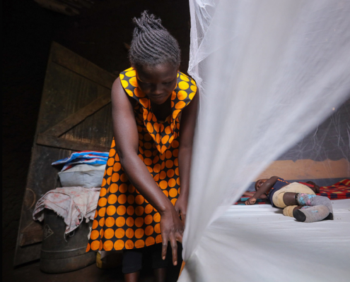 A mother secures her child under a mosquito net