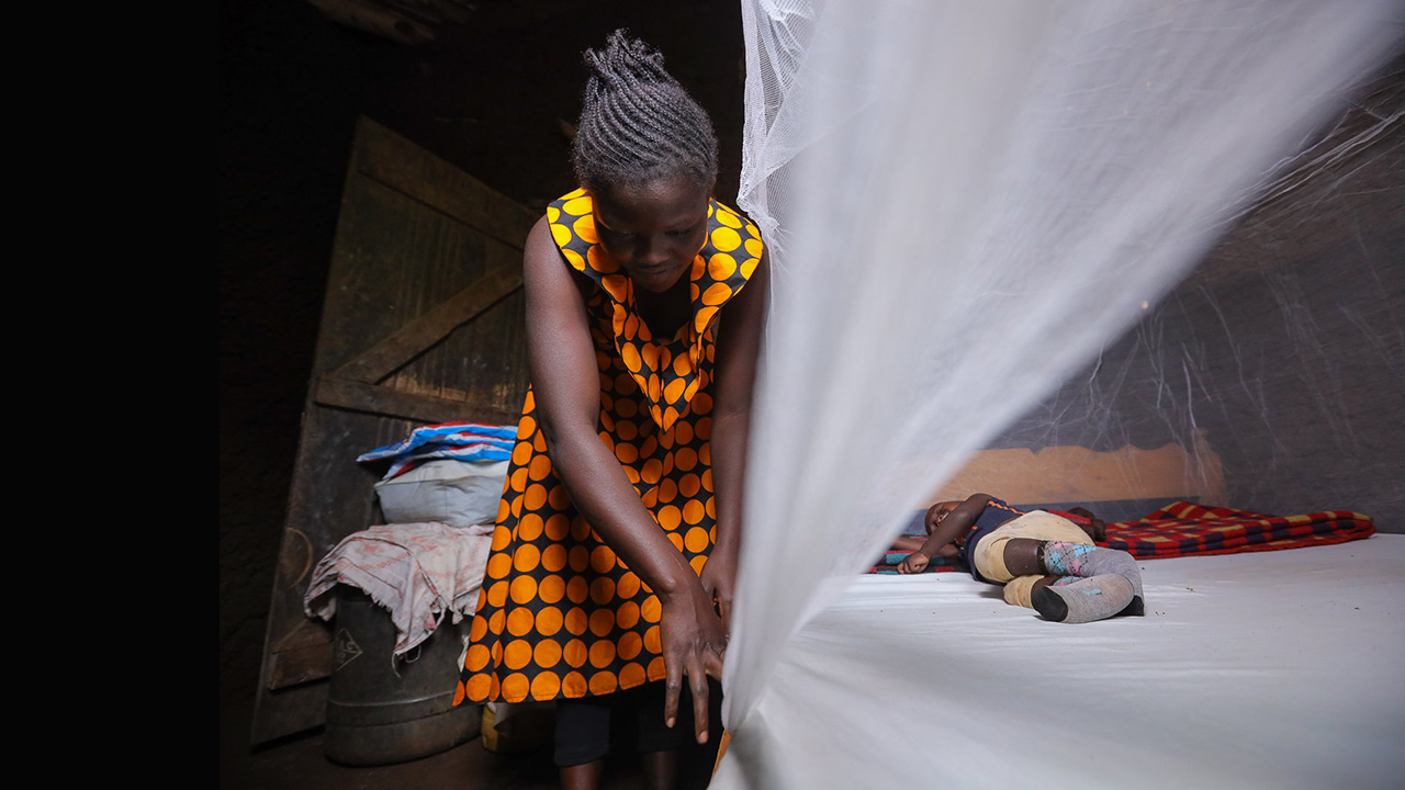 A mother secures her child under a mosquito net