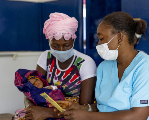A community health nurse gives medical advice to a mother holding an infant in Sierra Leone