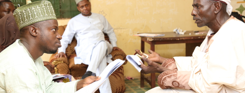 Two Nigerian men, seated across each other, having a conversation.