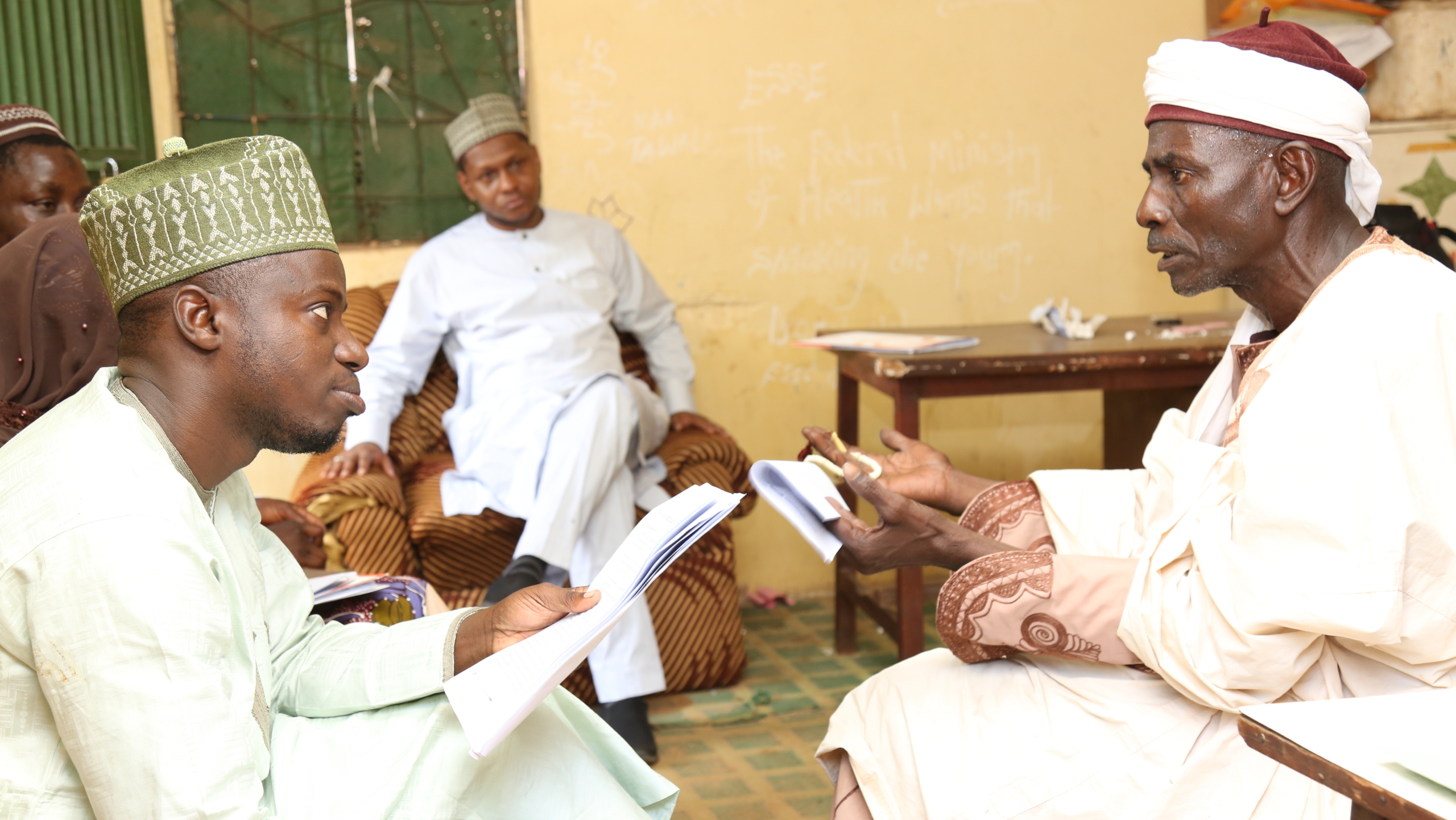 Two Nigerian men, seated across each other, having a conversation.