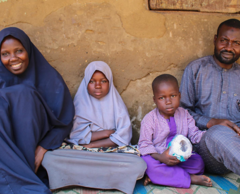 A Nigerian family, comprising a mother, a young girl, a young boy, and a father, sitting on the ground.