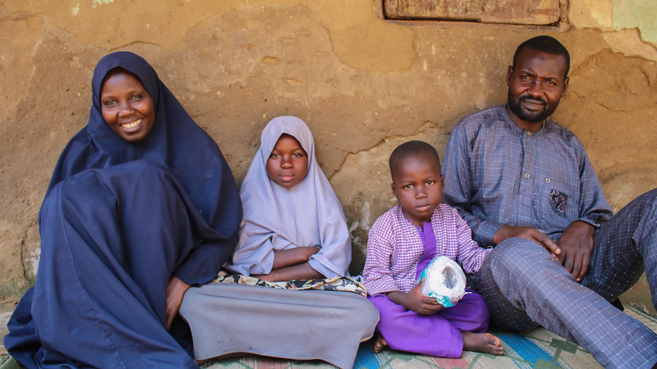 A Nigerian family, comprising a mother, a young girl, a young boy, and a father, sitting on the ground.