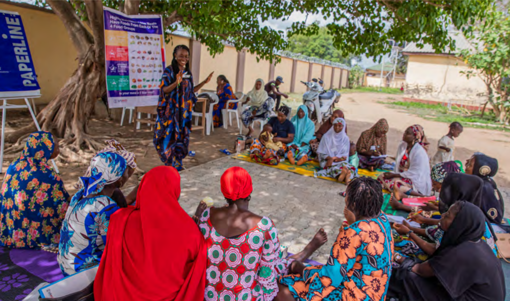 A group of Nigerian women who are part of a women's empowerment group sitting on the ground, under a tree.