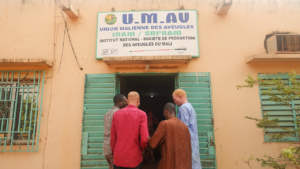 Three men standing in front of the main entrance to the Mali Union for the Blind office.