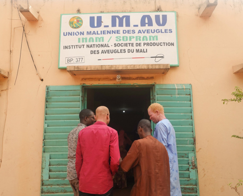 Three men standing in front of the main entrance to the Mali Union for the Blind office.