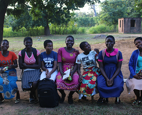 Seven adolescent girls smiling and sitting on a bench