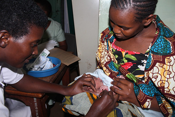 A health care provider vaccinates a newborn in its mother's arms