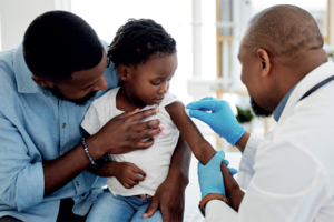 Father holds daughter as she gets the malaria vaccine from a male health care worker in the DRC