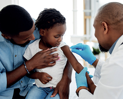 Father holds daughter as she gets the malaria vaccine from a male health care worker in the DRC