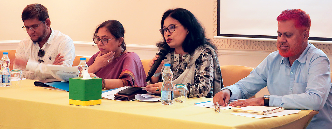 A woman speaks into a microphone at a panel with another woman and two men.