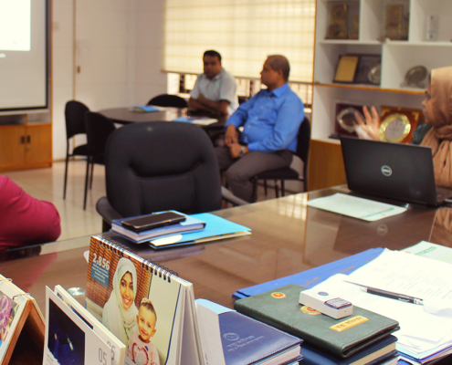 A woman makes a presentation to three men in an office setting.