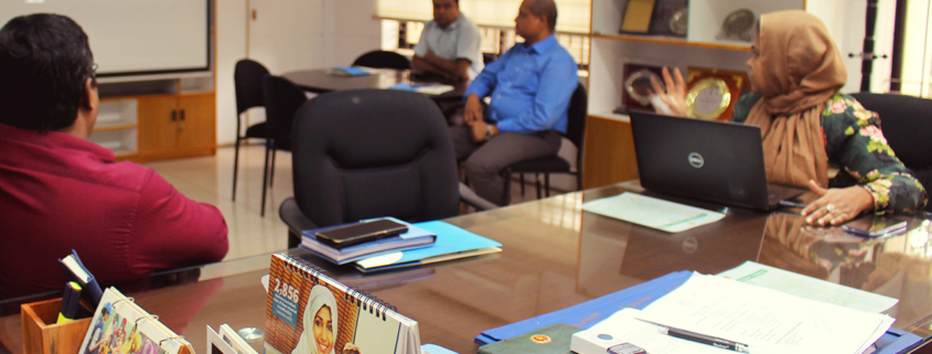 A woman makes a presentation to three men in an office setting.